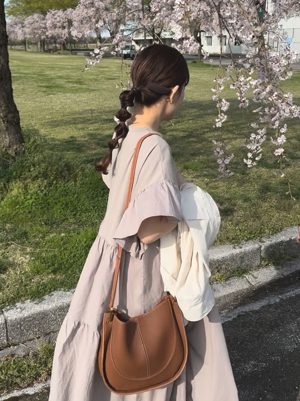 ベージュ系のワンピース、ブラウン系のショルダーバッグ、ブラック系のスニーカーを着用したレディースの春コーディネートの3枚目の写真