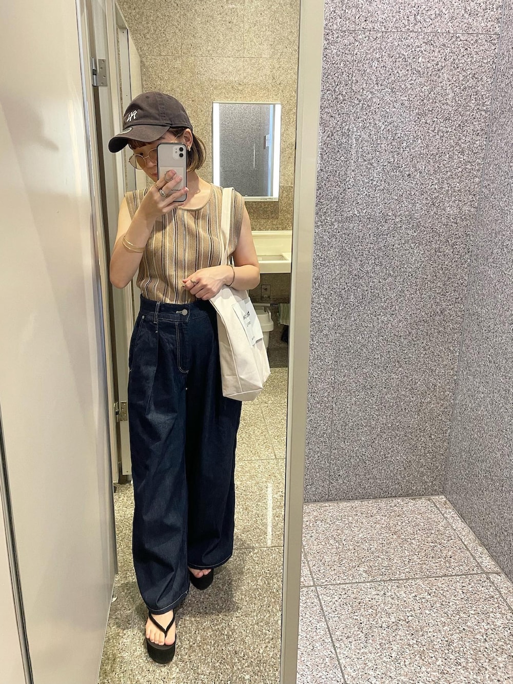 ベージュ系のタンクトップ、ブルー系のデニムパンツ、ホワイト系のトートバッグを着用したレディースの夏コーディネートの3枚目の写真