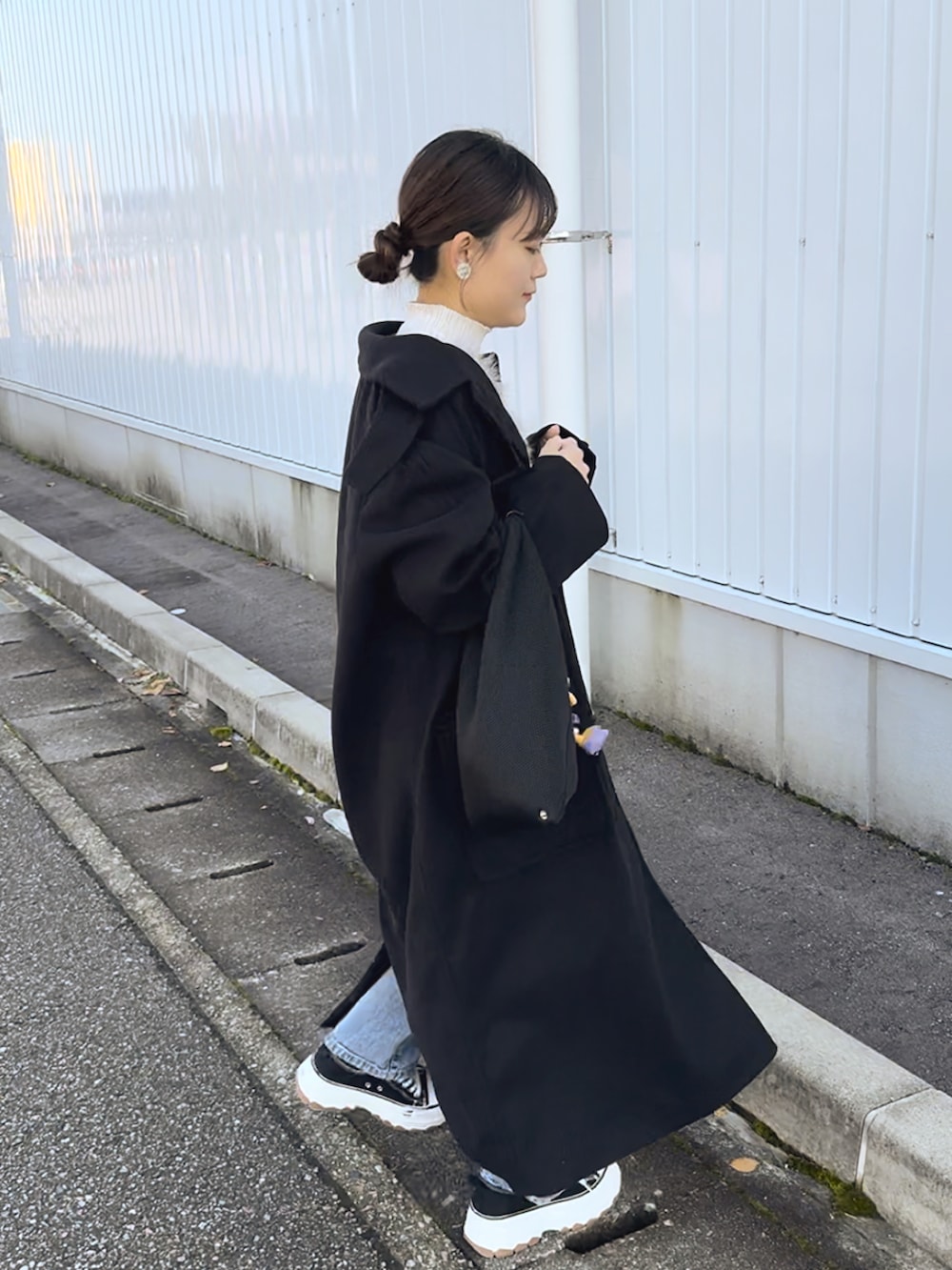 ブラック系のステンカラーコート、グレー系のベスト、ブルー系のデニムパンツを着用したレディースの冬コーディネートの4枚目の写真