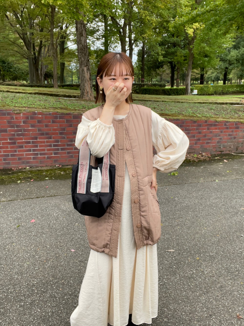 ベージュ系のベスト、ホワイト系のワンピース、ブラック系のショルダーバッグを着用したレディースの秋コーディネートの3枚目の写真