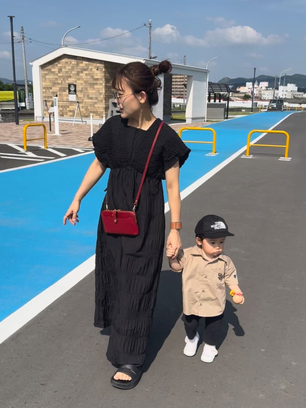 ブラック系のワンピース、ブラック系のサンダル、レッド系のショルダーバッグを着用したレディースの夏コーディネートの2枚目の写真