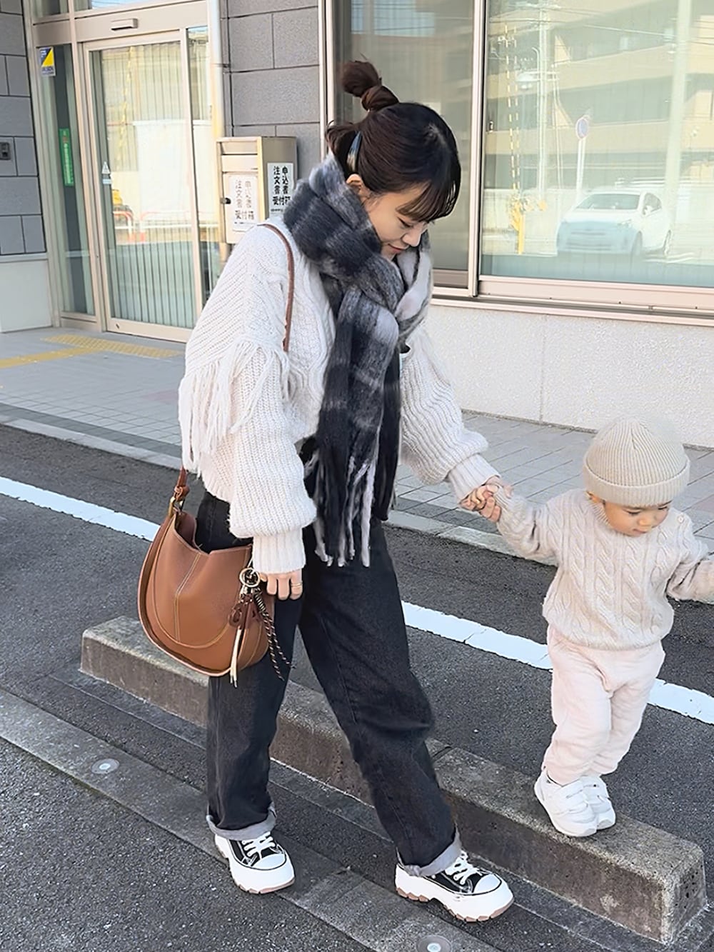 ブラウン系のショルダーバッグ、ホワイト系のニット/セーター、ブルー系のパンツを着用したレディースの冬コーディネートの2枚目の写真