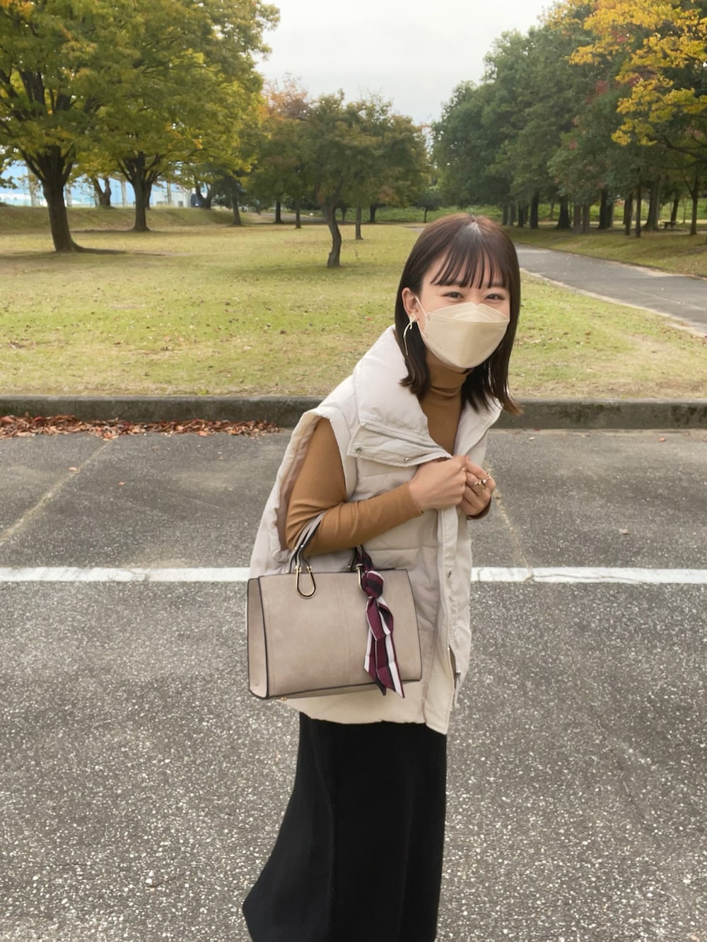 ベージュ系のバッグ、ホワイト系のダウンベスト、イエロー系のトップスを着用したレディースの秋コーディネートの3枚目の写真