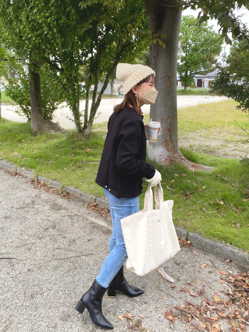ホワイト系のトートバッグ、ブラック系のブーツ、ブルー系のデニムパンツを着用したレディースの秋コーディネートの3枚目の写真