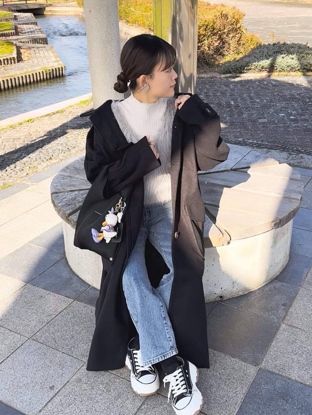 ブラック系のステンカラーコート、グレー系のベスト、ブルー系のデニムパンツを着用したレディースの冬コーディネートの2枚目の写真