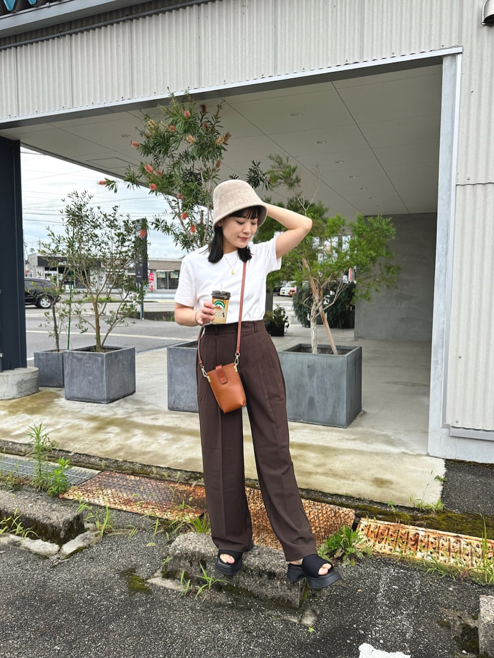 ホワイト系のトップス、ブラウン系のパンツ、ブラック系のサンダルを着用したレディースの夏コーディネートの3枚目の写真