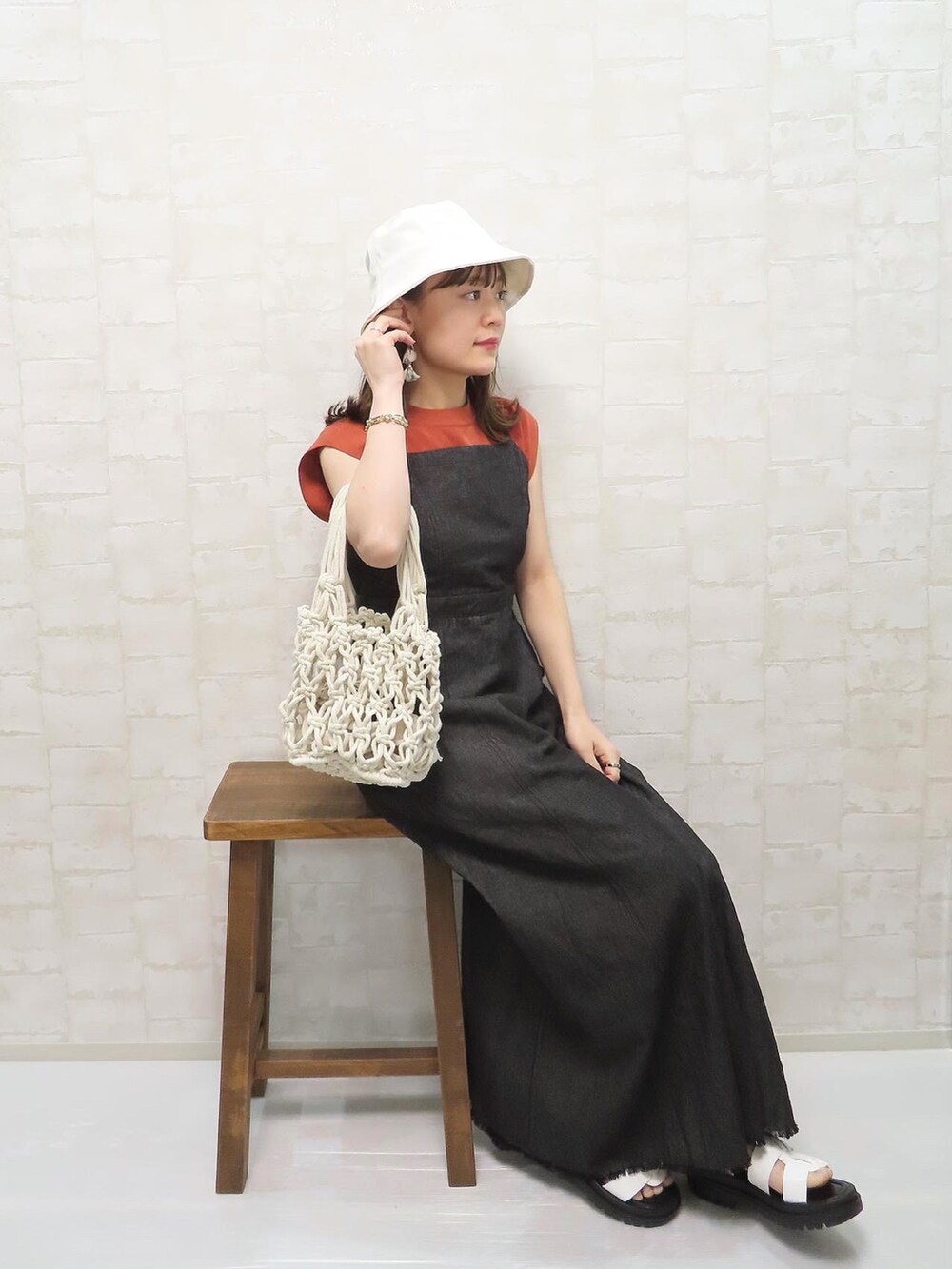 ブラック系のワンピース、オレンジ系のニット/セーター、ホワイト系のハットを着用したレディースの春コーディネートの4枚目の写真