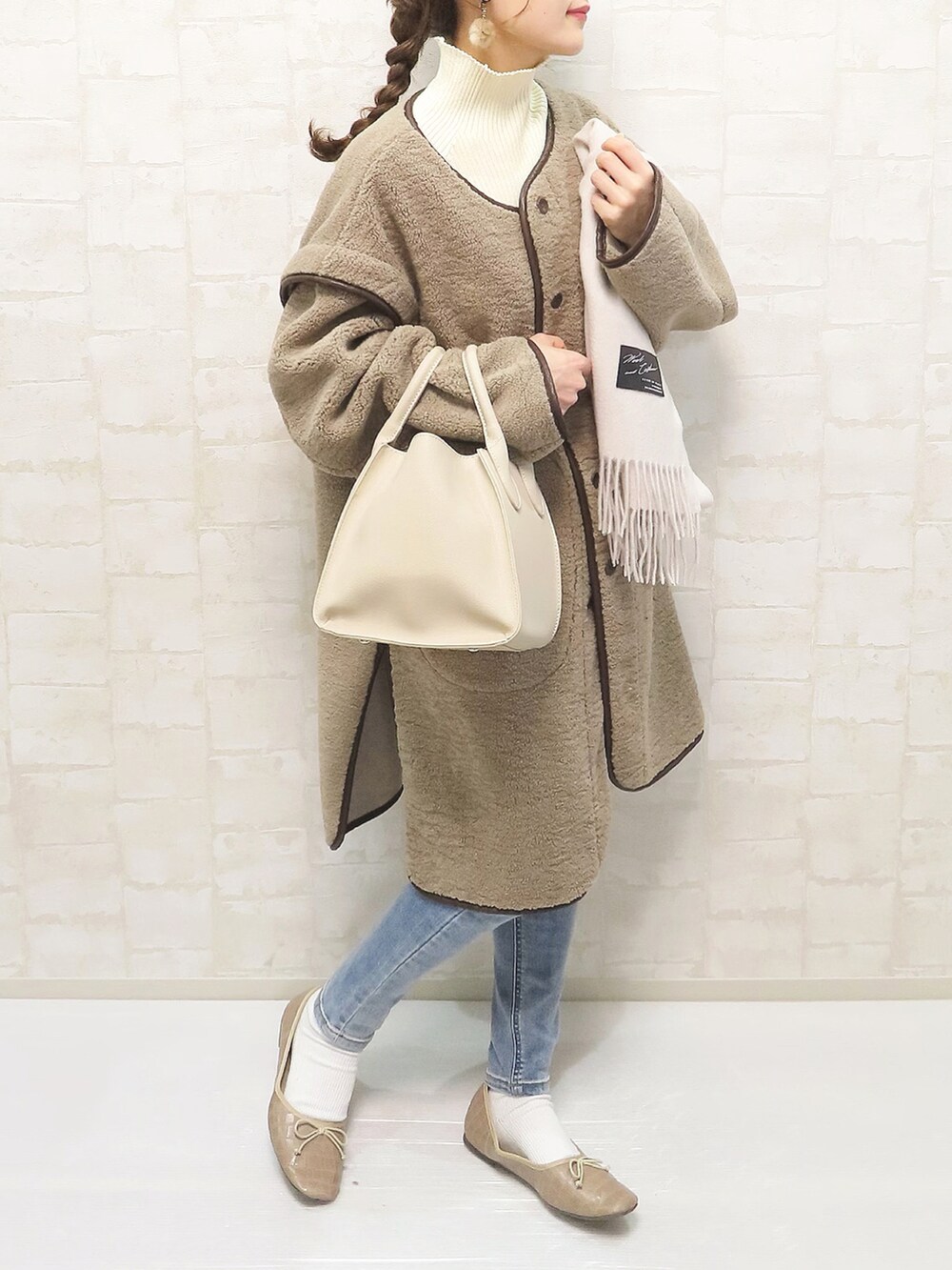 ベージュ系のムートンコート、ホワイト系のニット/セーター、ブルー系のデニムパンツを着用したレディースの秋コーディネートの2枚目の写真