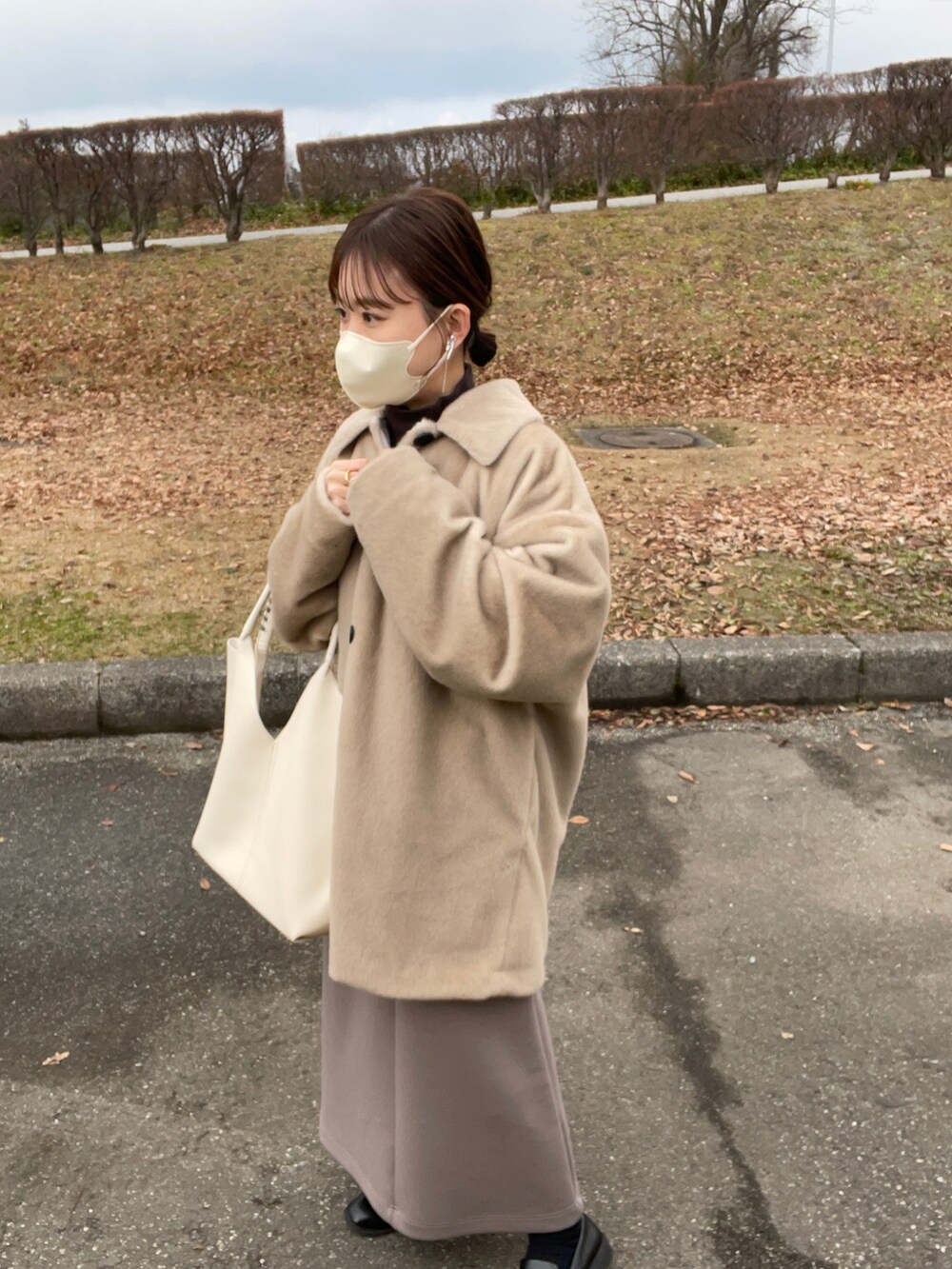 ブラウン系のワンピース、ホワイト系のトートバッグ、ベージュ系のステンカラーコートを着用したレディースの冬コーディネートの4枚目の写真