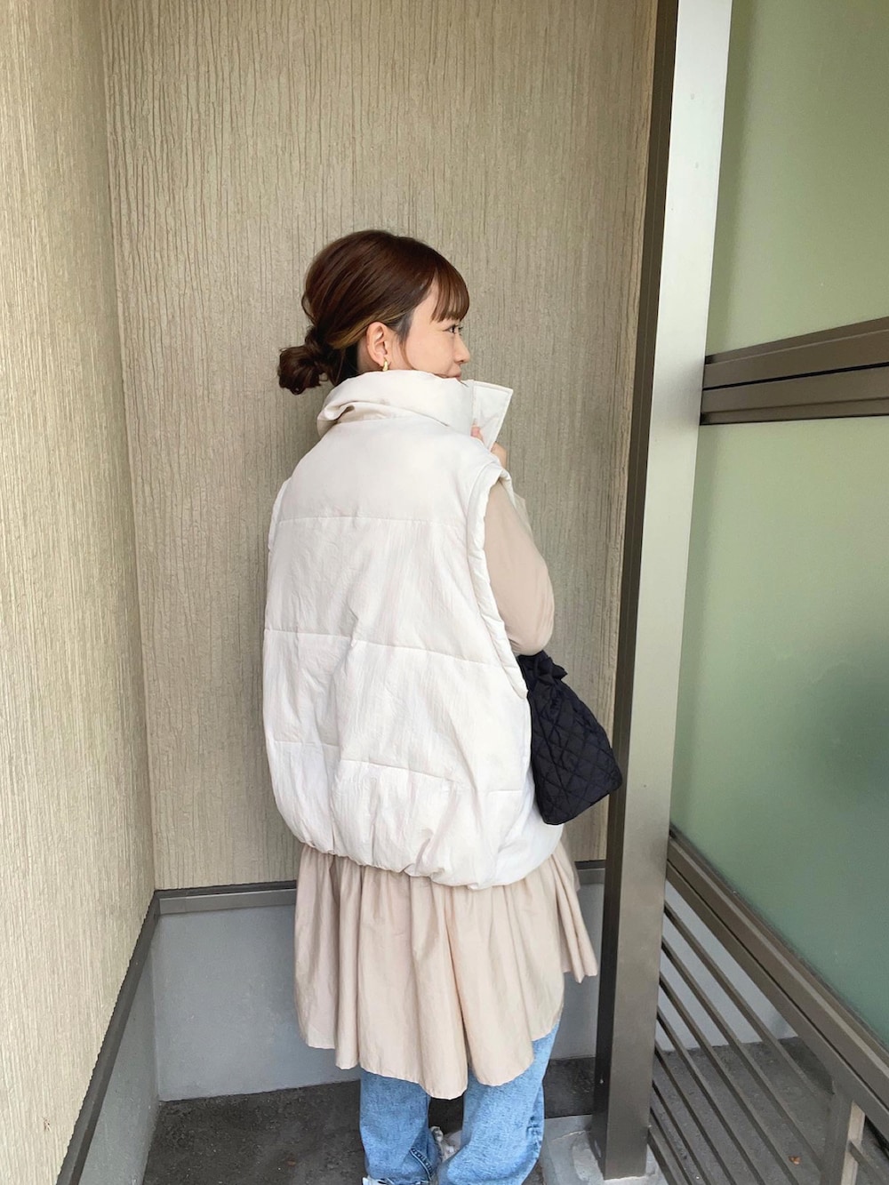 ベージュ系のワンピース、ホワイト系のダウンベスト、ブルー系のデニムパンツを着用したレディースの秋コーディネートの2枚目の写真