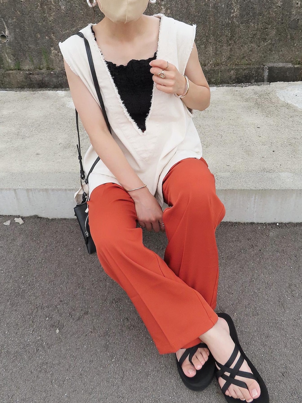 オレンジ系のスラックス、ホワイト系のベスト、ブラック系のタンクトップを着用したレディースの夏コーディネートの3枚目の写真