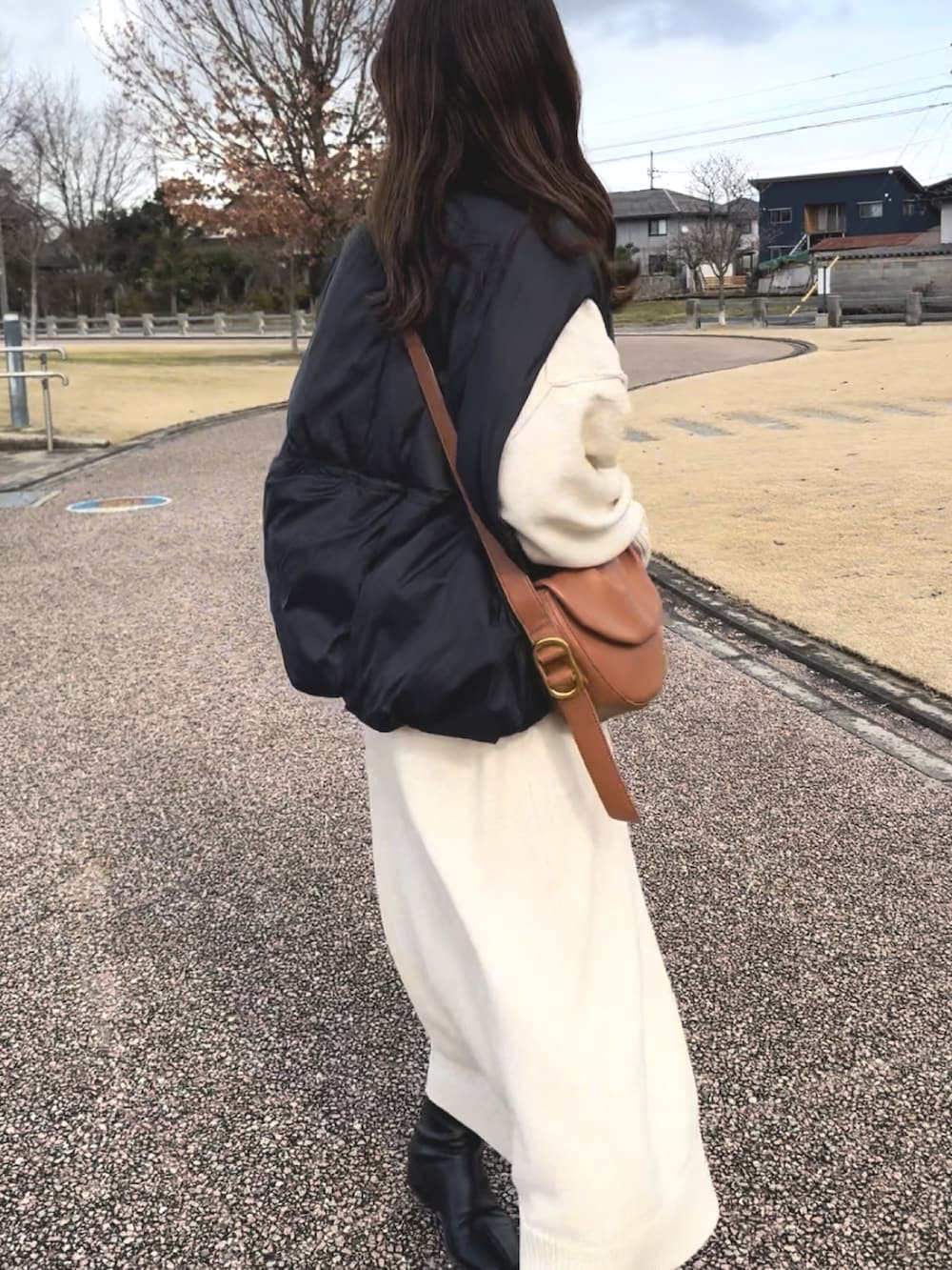 ブラック系のダウンベスト、ホワイト系のワンピース、ブラウン系のハンドバッグを着用したレディースの冬コーディネートの5枚目の写真