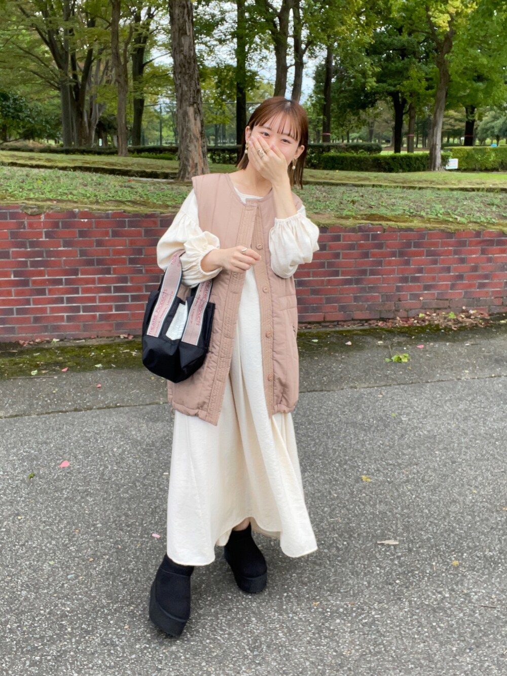 ベージュ系のベスト、ホワイト系のワンピース、ブラック系のショルダーバッグを着用したレディースの秋コーディネートの5枚目の写真