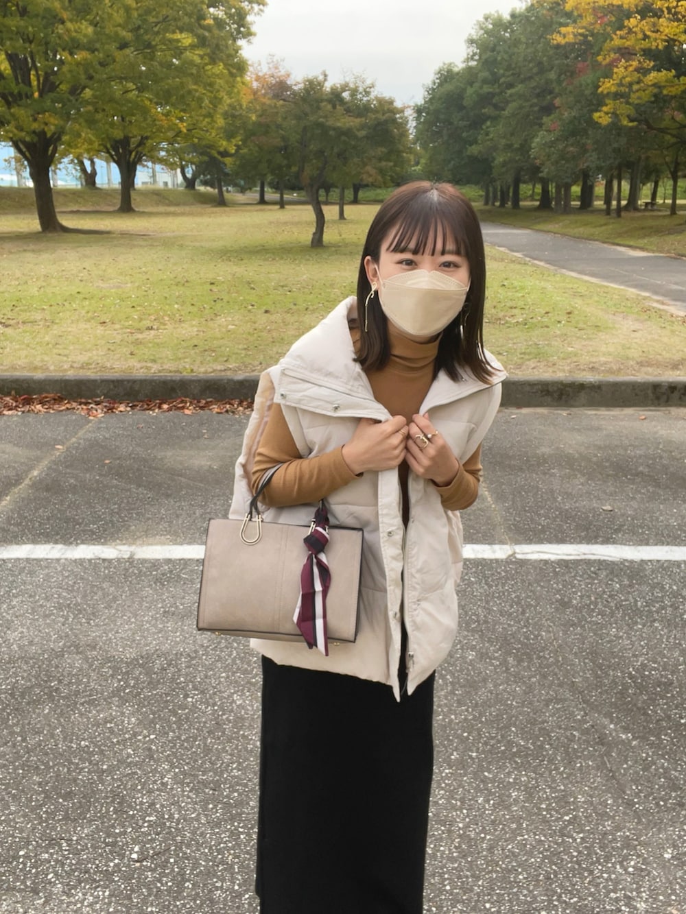 ベージュ系のバッグ、ホワイト系のダウンベスト、イエロー系のトップスを着用したレディースの秋コーディネートの5枚目の写真