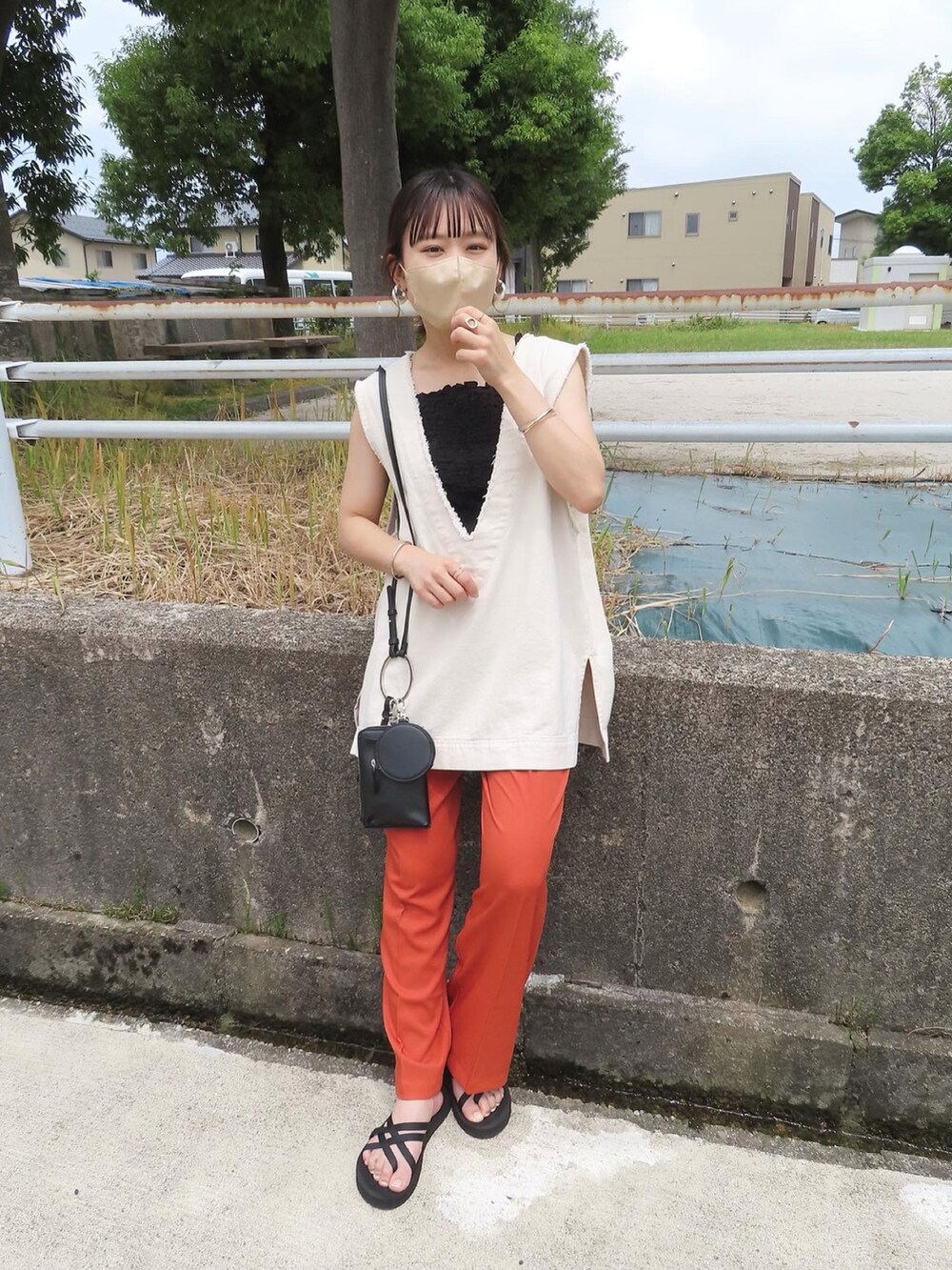 オレンジ系のスラックス、ホワイト系のベスト、ブラック系のタンクトップを着用したレディースの夏コーディネートの2枚目の写真