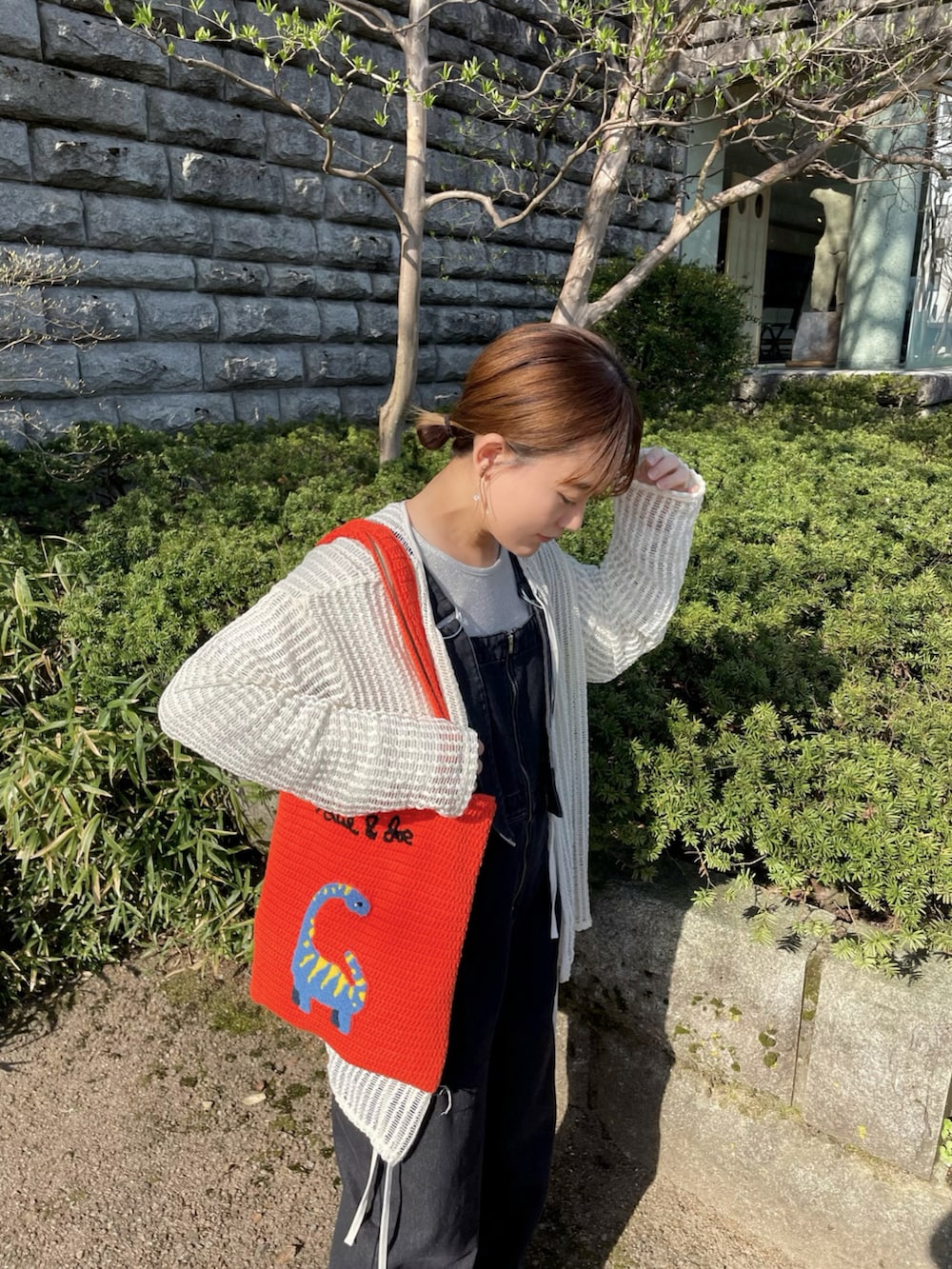 オレンジ系のトートバッグ、シルバー系のトップス、ホワイト系のカーディガン/ボレロを着用したレディースの春コーディネートの2枚目の写真