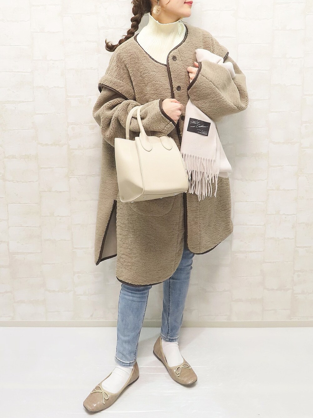 ベージュ系のムートンコート、ホワイト系のニット/セーター、ブルー系のデニムパンツを着用したレディースの秋コーディネートの3枚目の写真