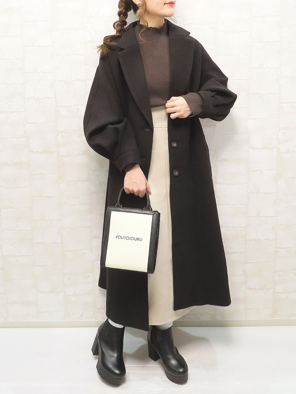 ブラック系のチェスターコート、ブラウン系のニット/セーター、ベージュ系のスカートを着用したレディースの秋コーディネートの2枚目の写真