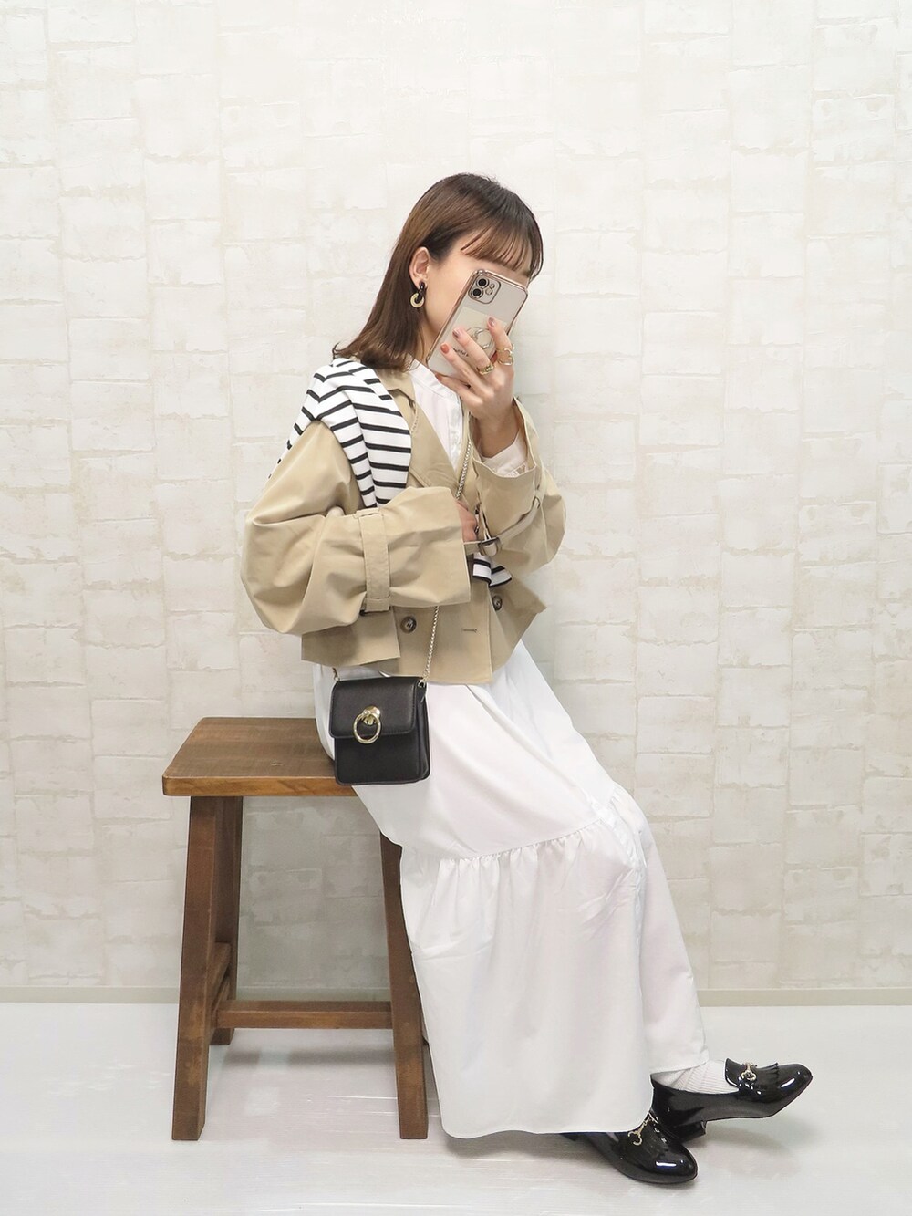 ベージュ系のトレンチコート、ホワイト系のワンピース/ドレス、ブラック系のショルダーバッグを着用したレディースの春コーディネートの2枚目の写真