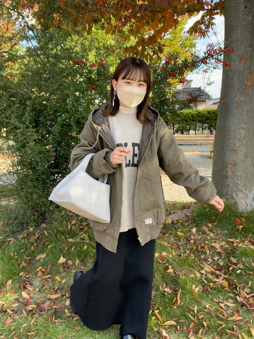 グリーン系のブルゾン、ホワイト系のニット/セーター、ベージュ系のバッグを着用したレディースの秋コーディネートの3枚目の写真