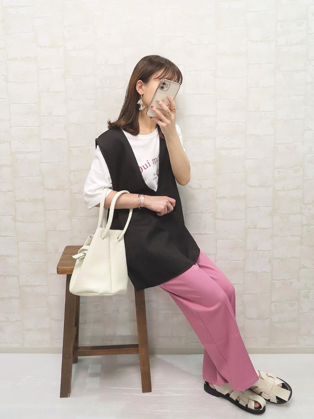 ピンク系のスラックス、ブラック系のベスト、ホワイト系のハンドバッグを着用したレディースの夏コーディネートの2枚目の写真