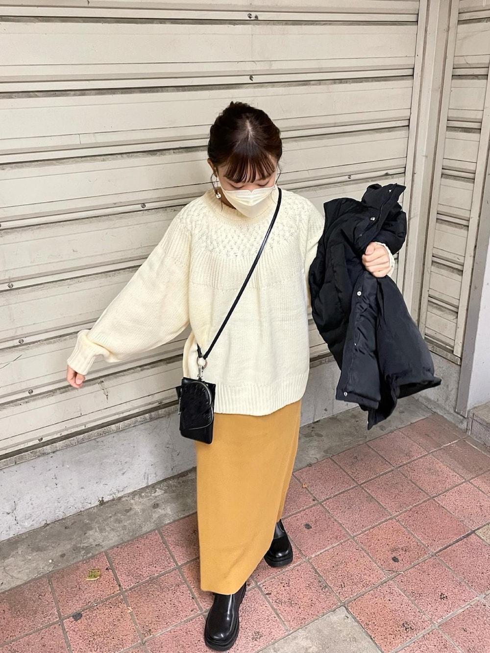 ホワイト系のニット/セーター、ブラック系のダウンベスト、イエロー系のスカートを着用したレディースの秋コーディネートの3枚目の写真