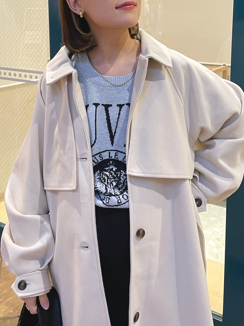 ホワイト系のステンカラーコート、グレー系のニット/セーター、ブラック系のハンドバッグを着用したレディースの冬コーディネートの3枚目の写真