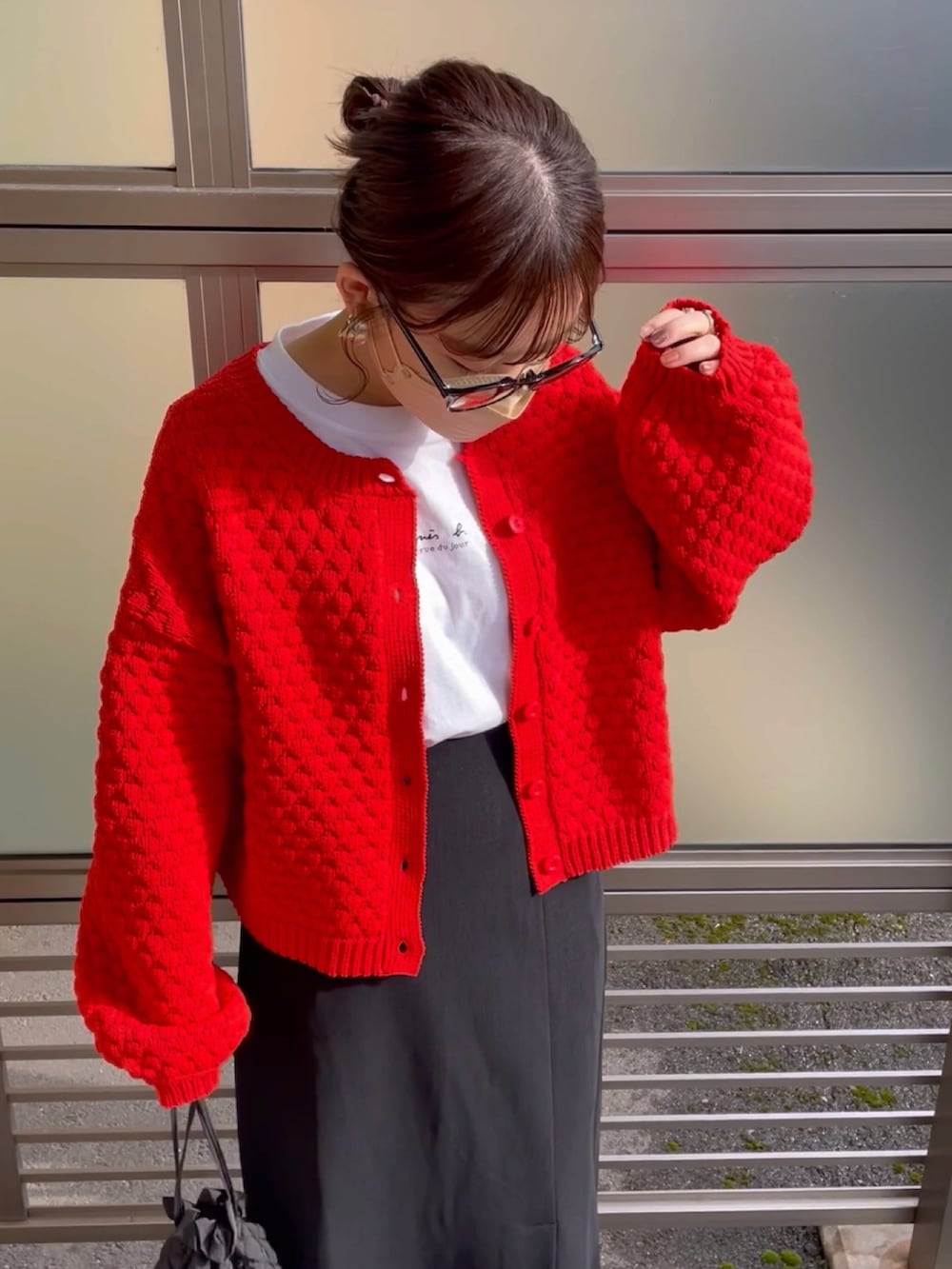 オレンジ系のカーディガン/ボレロ、ホワイト系のダウンベスト、ブラック系のスカートを着用したレディースの冬コーディネートの2枚目の写真