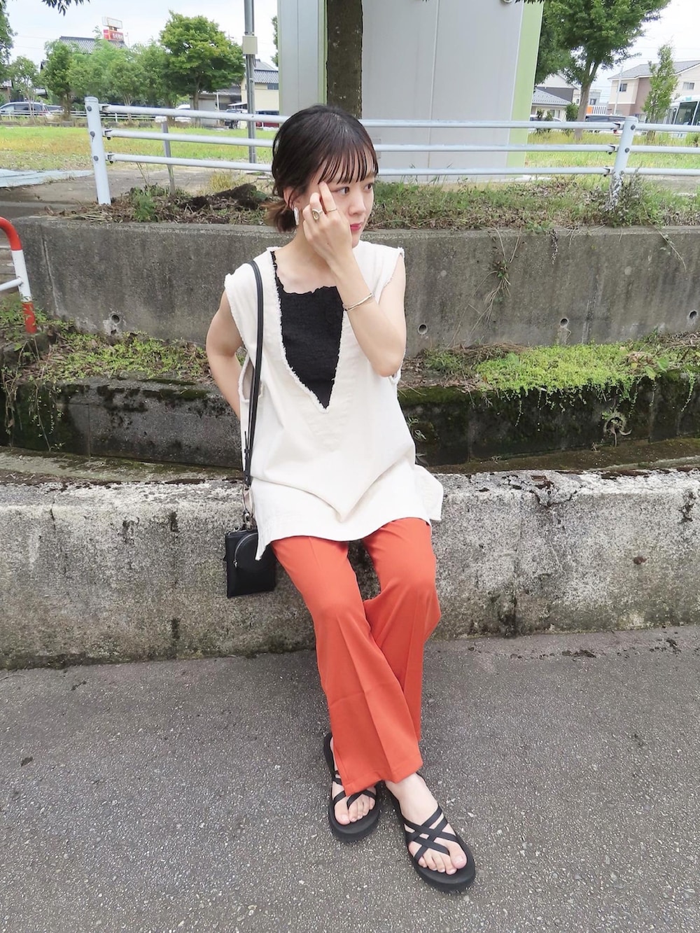 オレンジ系のスラックス、ホワイト系のベスト、ブラック系のタンクトップを着用したレディースの夏コーディネートの5枚目の写真