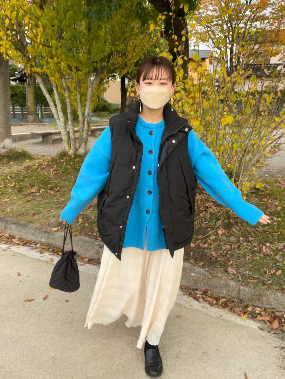 ベージュ系のスカート、ブルー系のカーディガン/ボレロ、ブラック系のダウンベストを着用したレディースの秋コーディネートの5枚目の写真