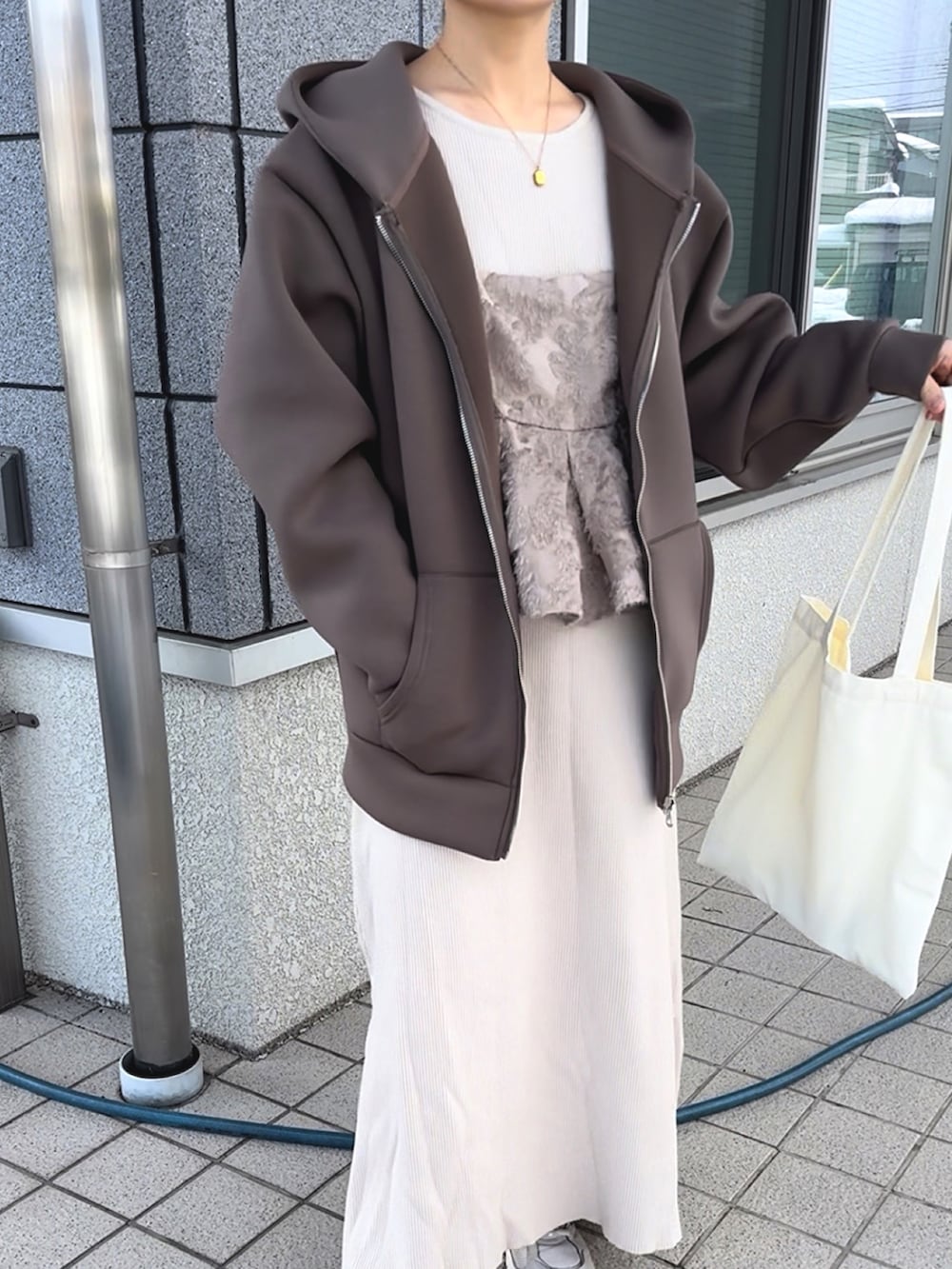 ブラウン系のパーカー、ベージュ系のワンピース、ホワイト系のトートバッグを着用したレディースの冬コーディネートの3枚目の写真