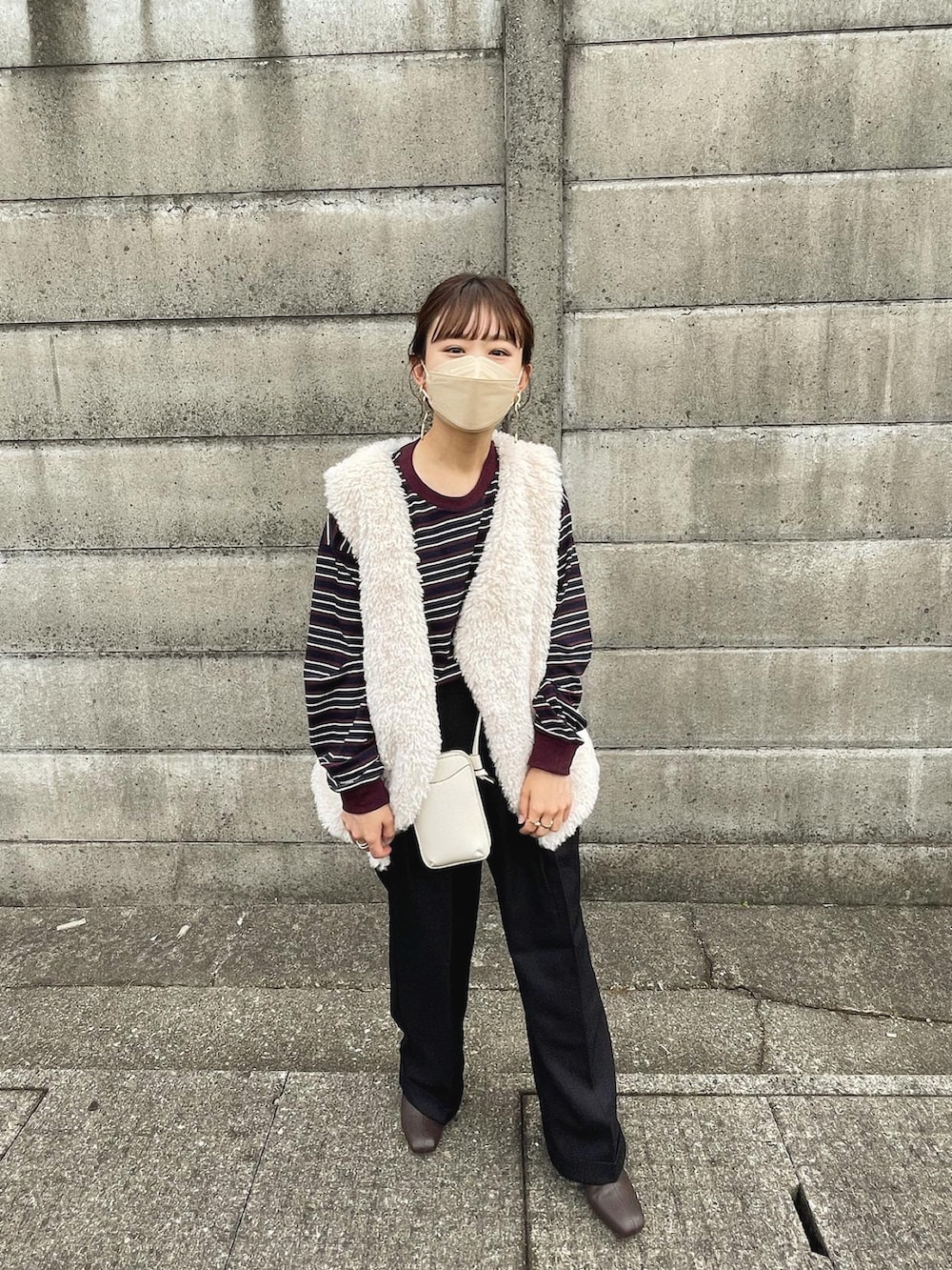 レッド系のトップス、ブラック系のパンツ、グレー系のベストを着用したレディースの秋コーディネートの5枚目の写真