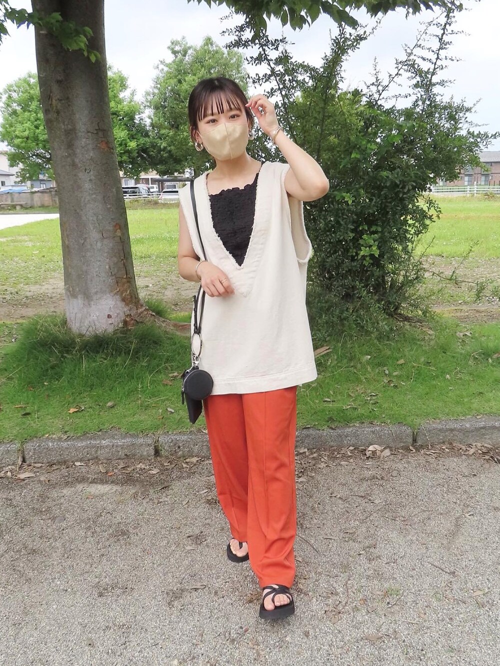 オレンジ系のスラックス、ホワイト系のベスト、ブラック系のタンクトップを着用したレディースの夏コーディネートの4枚目の写真