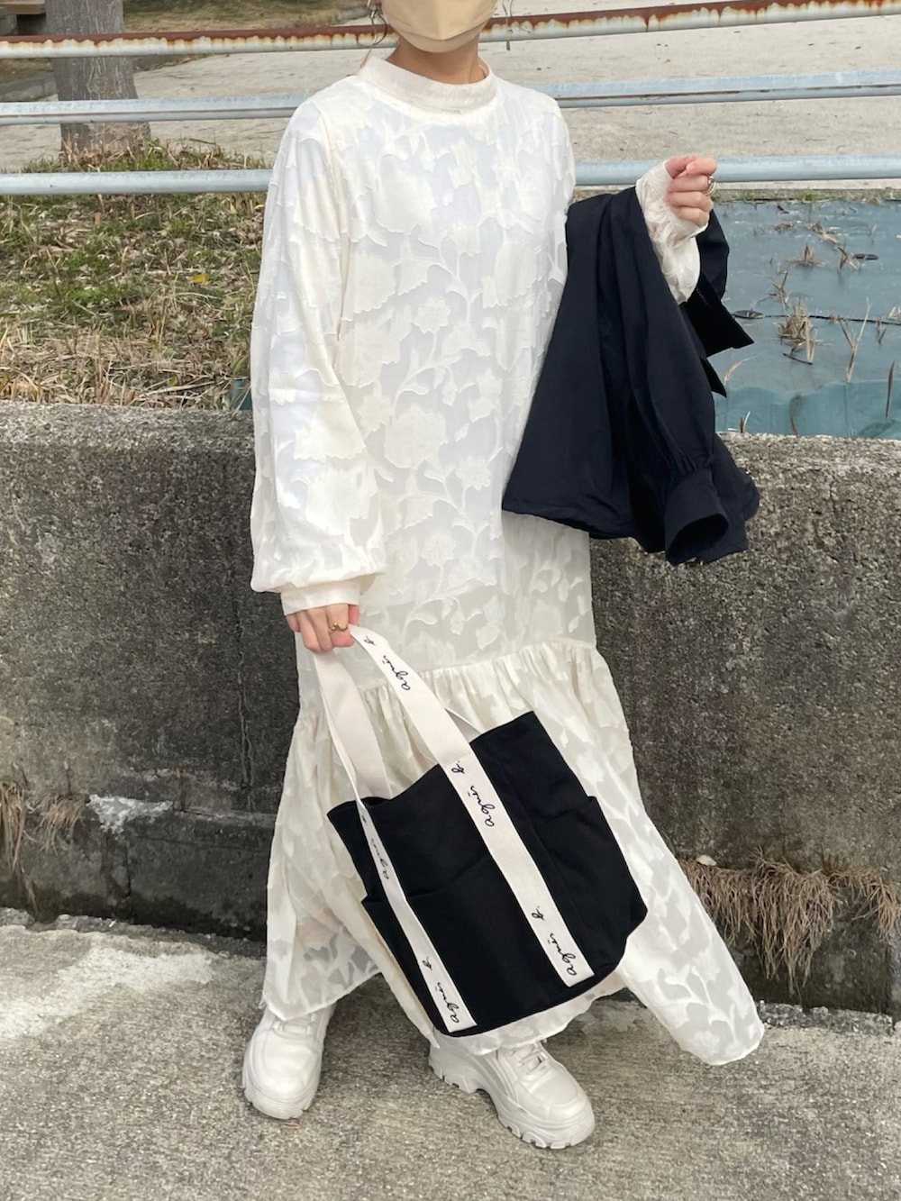 ホワイト系のドレス、ブラック系のトートバッグ、ブラック系のマウンテンパーカーを着用したレディースの冬コーディネートの4枚目の写真