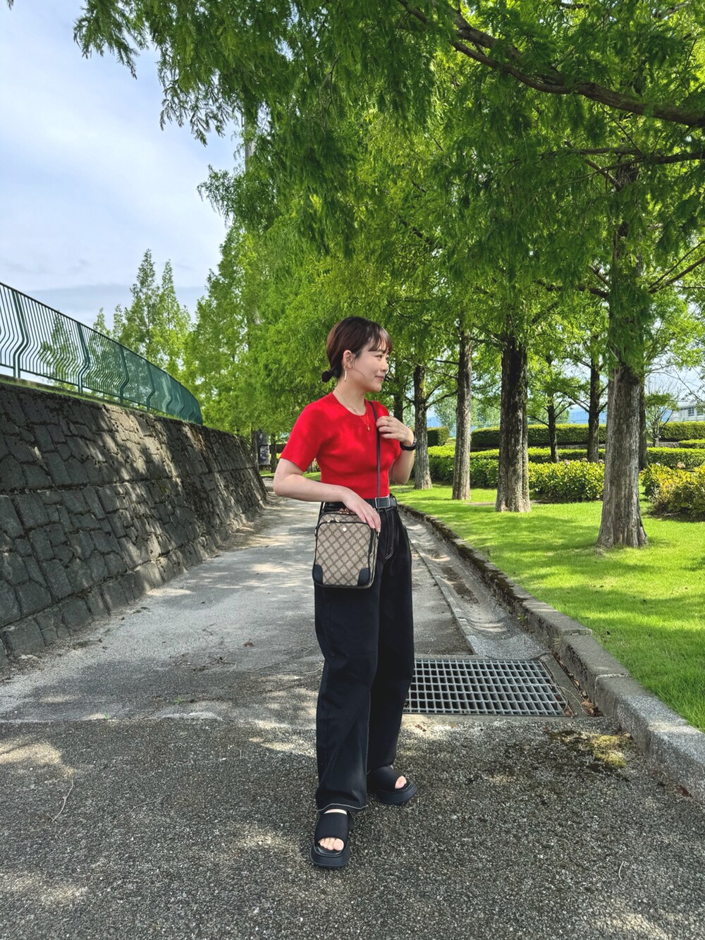 ブラック系のデニムパンツ、レッド系のトップス、ブラック系のショルダーバッグを着用したレディースの夏コーディネートの4枚目の写真