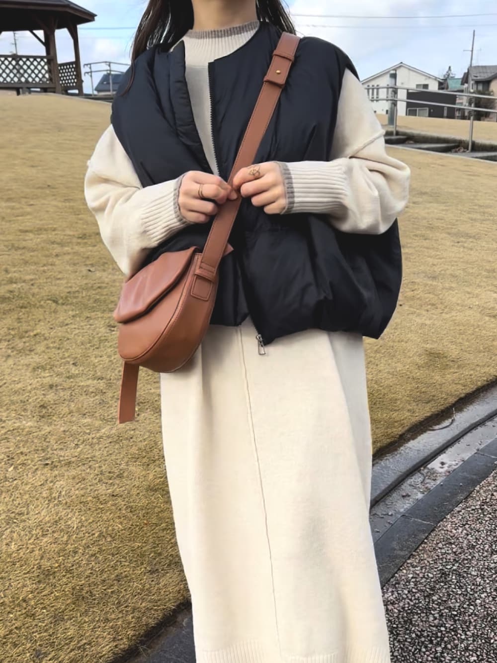 ブラック系のダウンベスト、ホワイト系のワンピース、ブラウン系のハンドバッグを着用したレディースの冬コーディネートの4枚目の写真