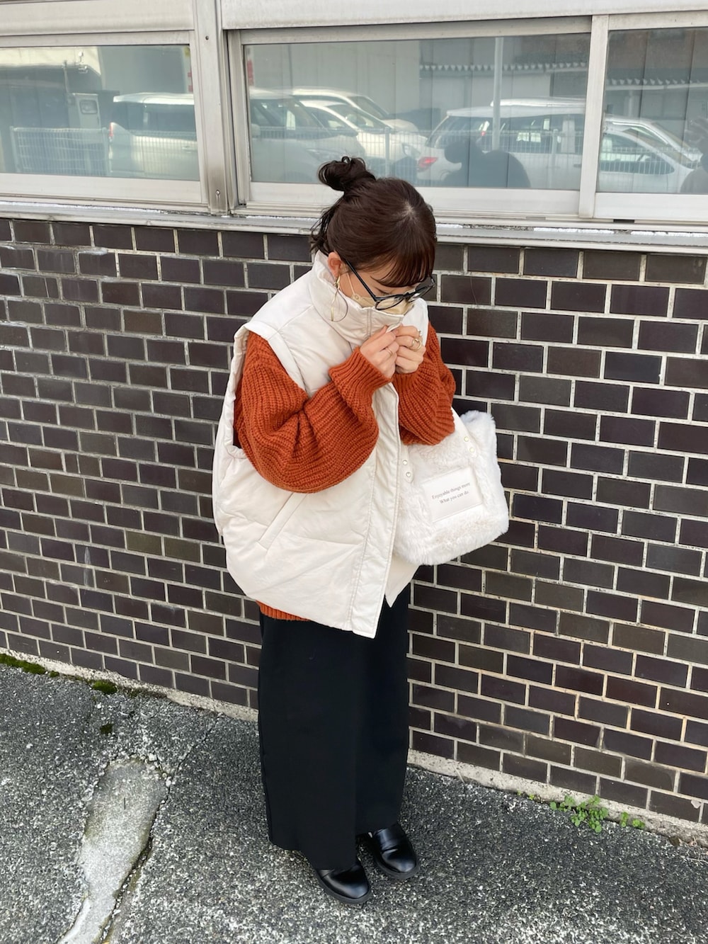 イエロー系のニット/セーター、ホワイト系のダウンベスト、ブラック系のスカートを着用したレディースの秋コーディネートの4枚目の写真