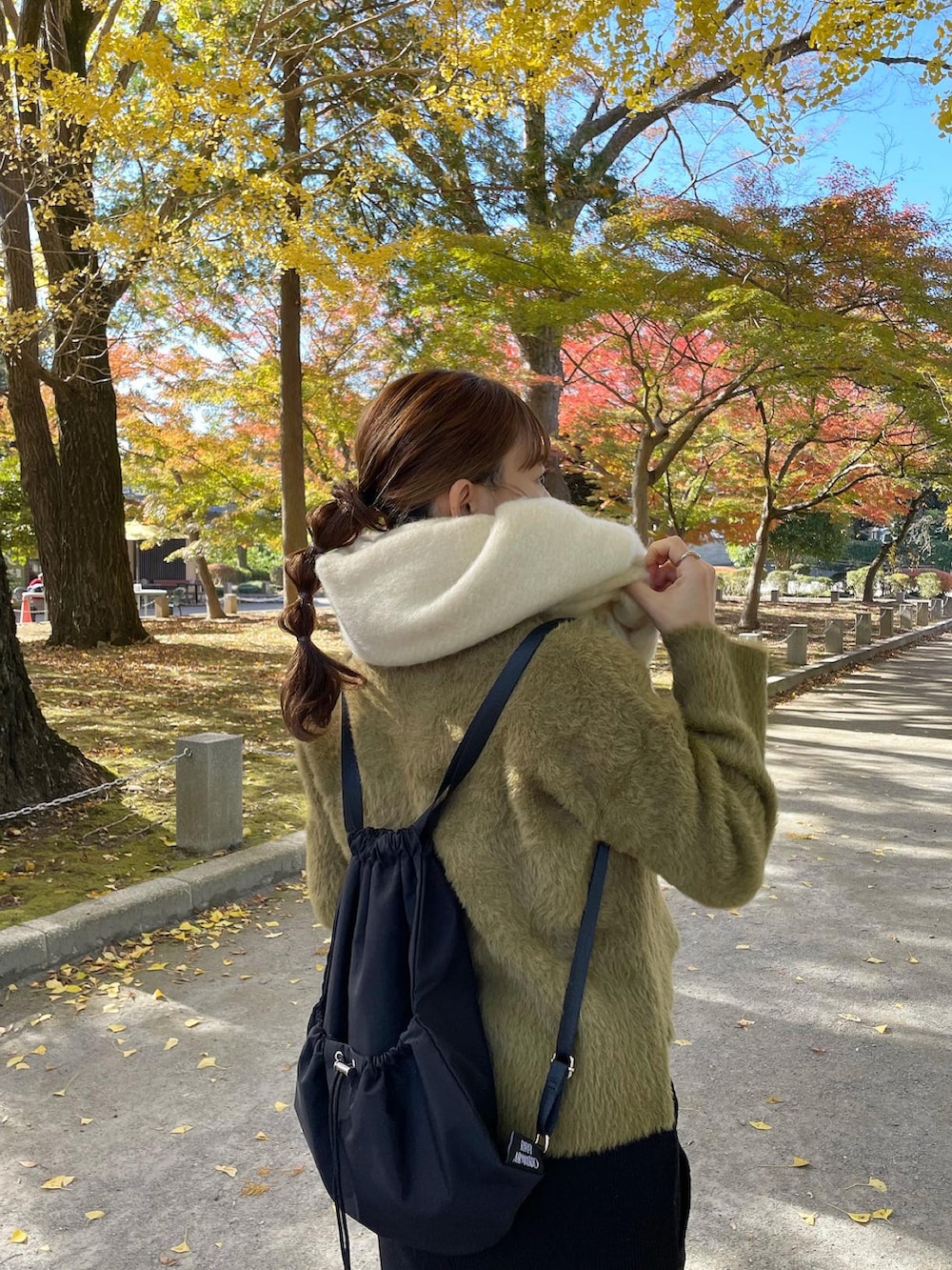 グリーン系のニット/セーター、ブラック系のバックパック/リュック、ホワイト系のスニーカーを着用したレディースの秋コーディネートの3枚目の写真