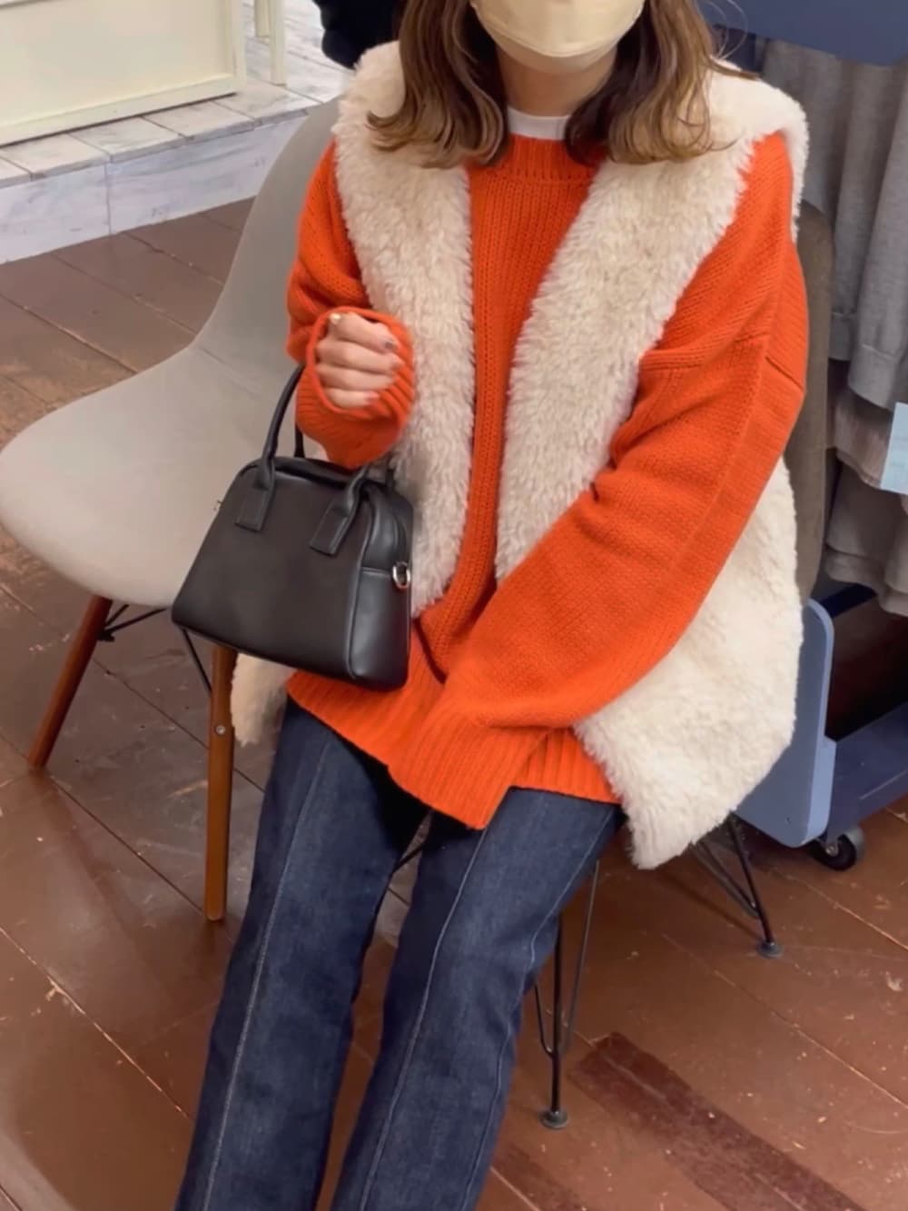 オレンジ系のカーディガン/ボレロ、グレー系のベスト、ブラック系のデニムパンツを着用したレディースの冬コーディネートの2枚目の写真