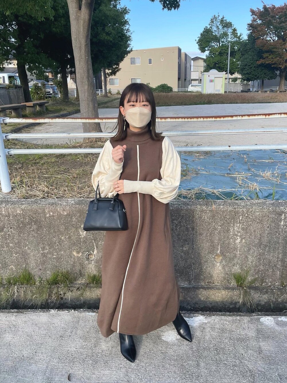 ブラウン系のワンピース、ブラック系のボストンバッグ、ブラック系のブーツを着用したレディースの秋コーディネートの3枚目の写真