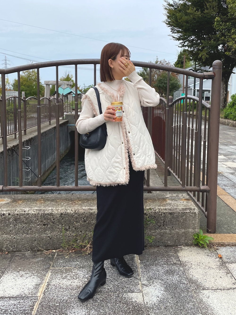ホワイト系のベスト、ブラック系のバッグ、ブラック系のブーツを着用したレディースの秋コーディネートの4枚目の写真