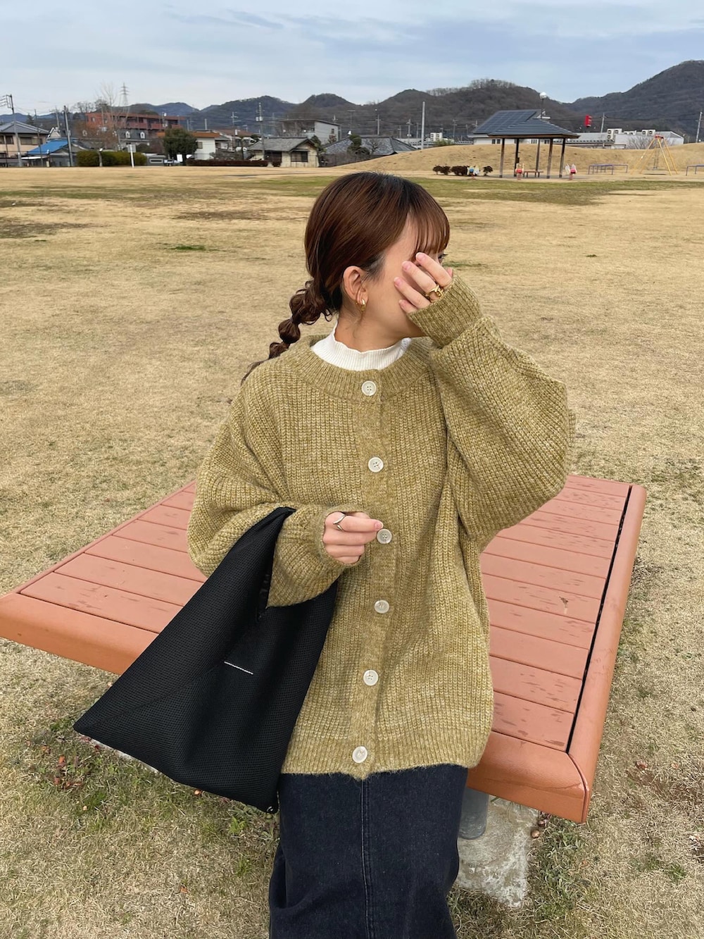 グリーン系のニット/セーター、ブラック系のデニムスカート、ブラック系のトートバッグを着用したレディースの冬コーディネートの2枚目の写真