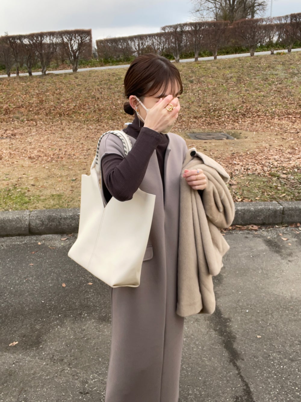 ブラウン系のワンピース、ホワイト系のトートバッグ、ベージュ系のステンカラーコートを着用したレディースの冬コーディネートの2枚目の写真