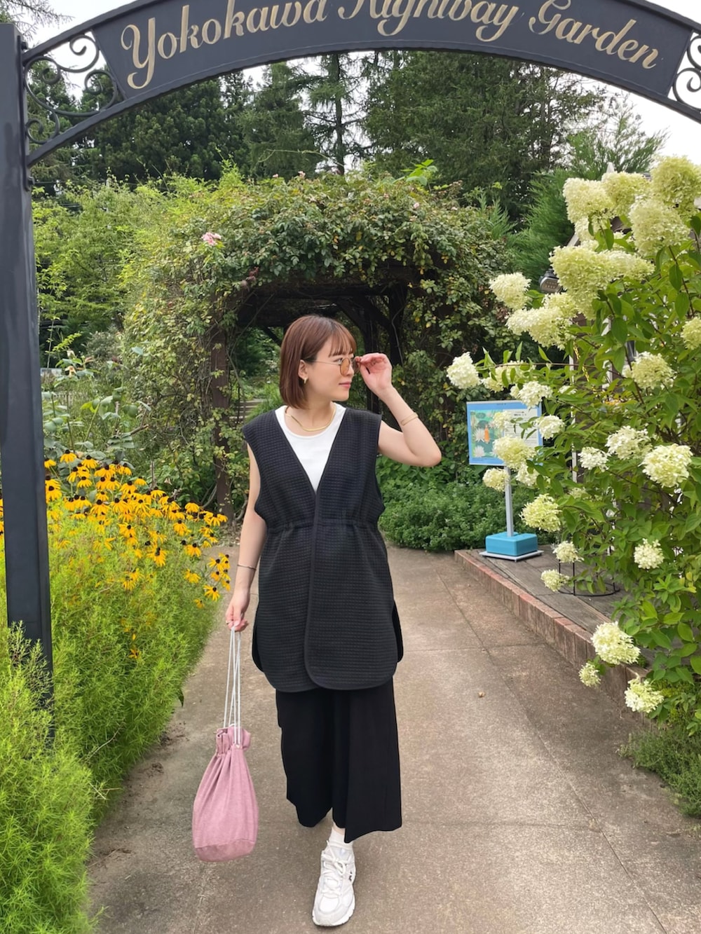 ブラック系のベスト、ホワイト系のタンクトップ、ピンク系のショルダーバッグを着用したレディースの夏コーディネートの2枚目の写真