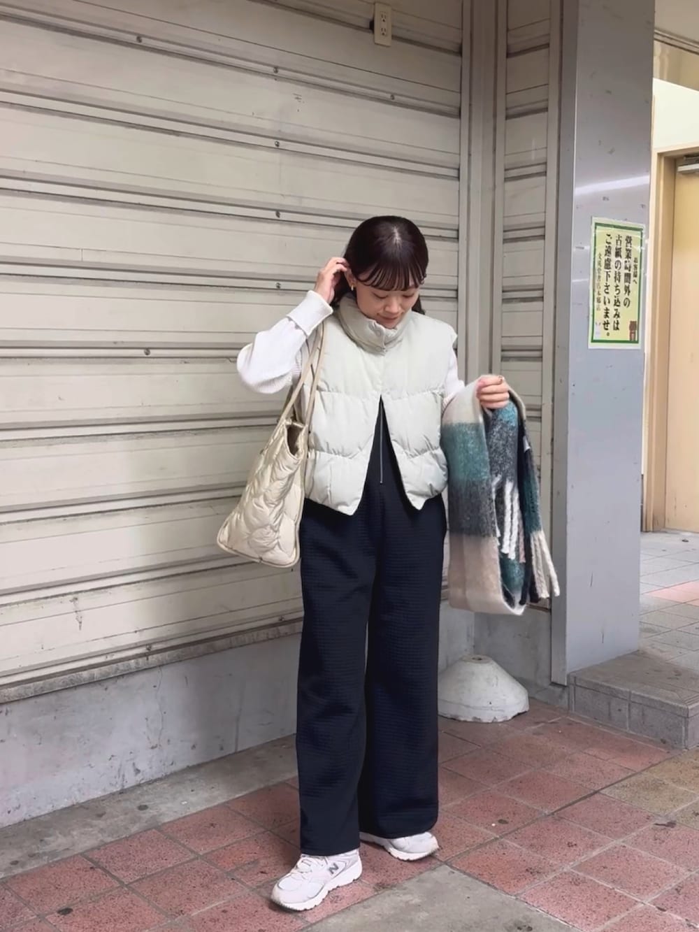 ベージュ系のダウンベスト、ブラック系のパンツ、ホワイト系のトートバッグを着用したレディースの冬コーディネートの3枚目の写真