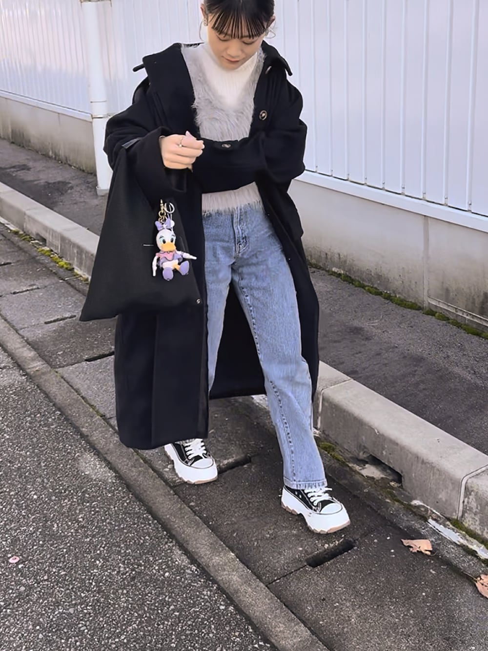 ブラック系のステンカラーコート、グレー系のベスト、ブルー系のデニムパンツを着用したレディースの冬コーディネートの5枚目の写真