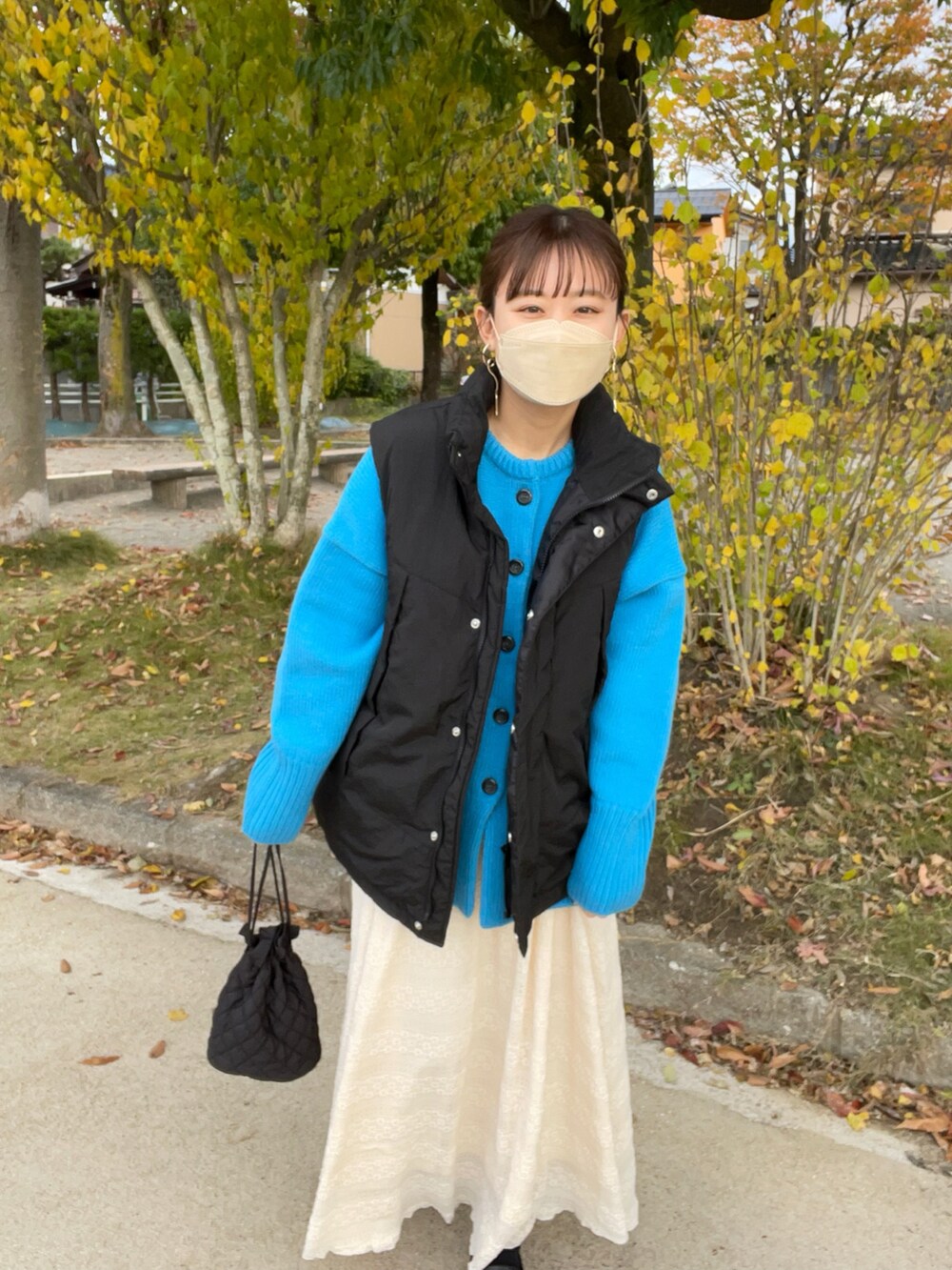 ベージュ系のスカート、ブルー系のカーディガン/ボレロ、ブラック系のダウンベストを着用したレディースの秋コーディネートの2枚目の写真