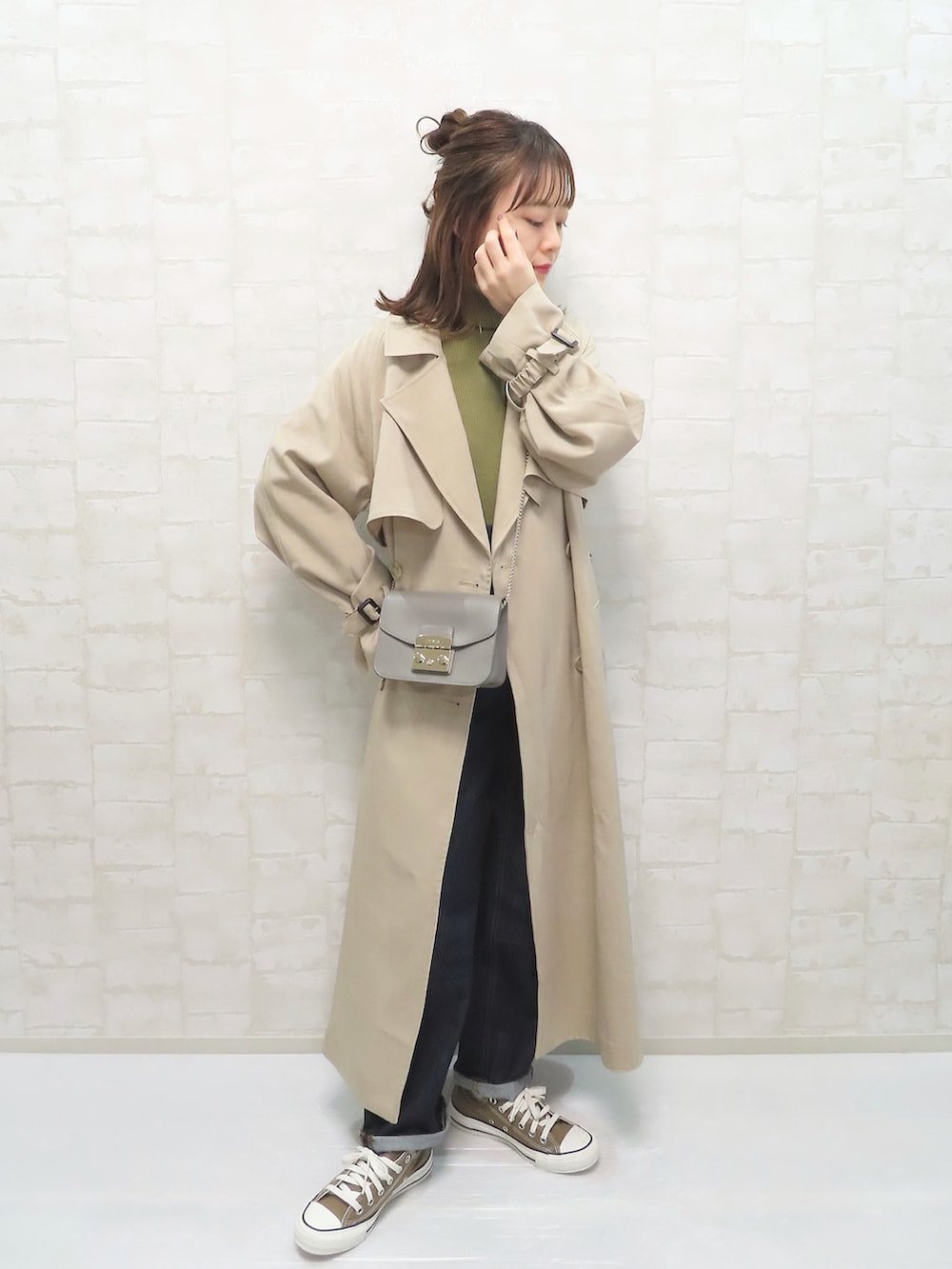 ベージュ系のトレンチコート、グリーン系のニット/セーター、ブルー系のデニムパンツを着用したレディースの冬コーディネートの2枚目の写真