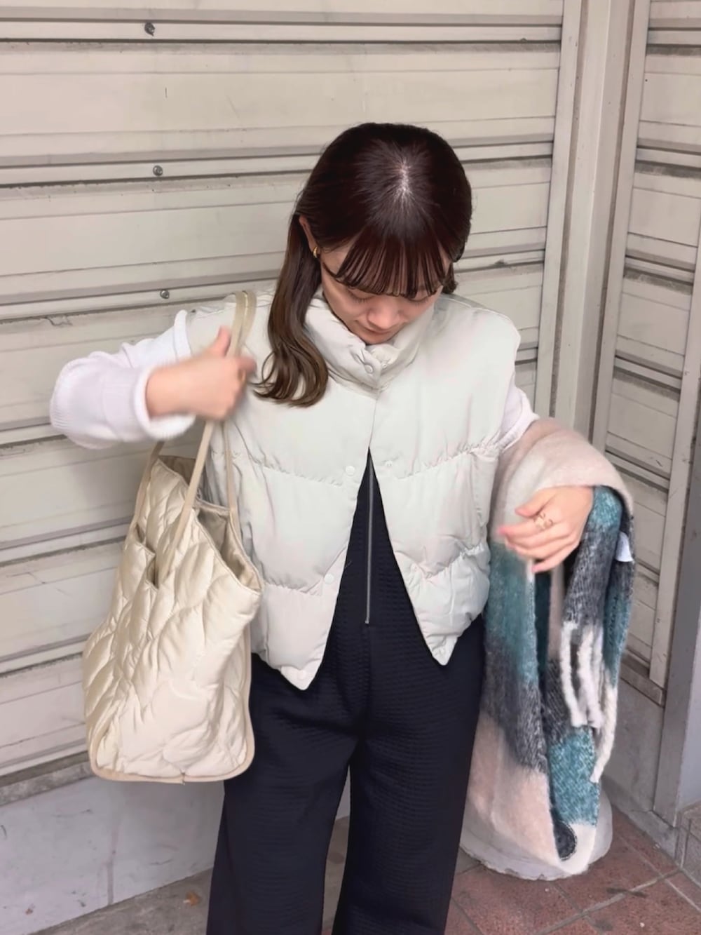 ベージュ系のダウンベスト、ブラック系のパンツ、ホワイト系のトートバッグを着用したレディースの冬コーディネートの2枚目の写真