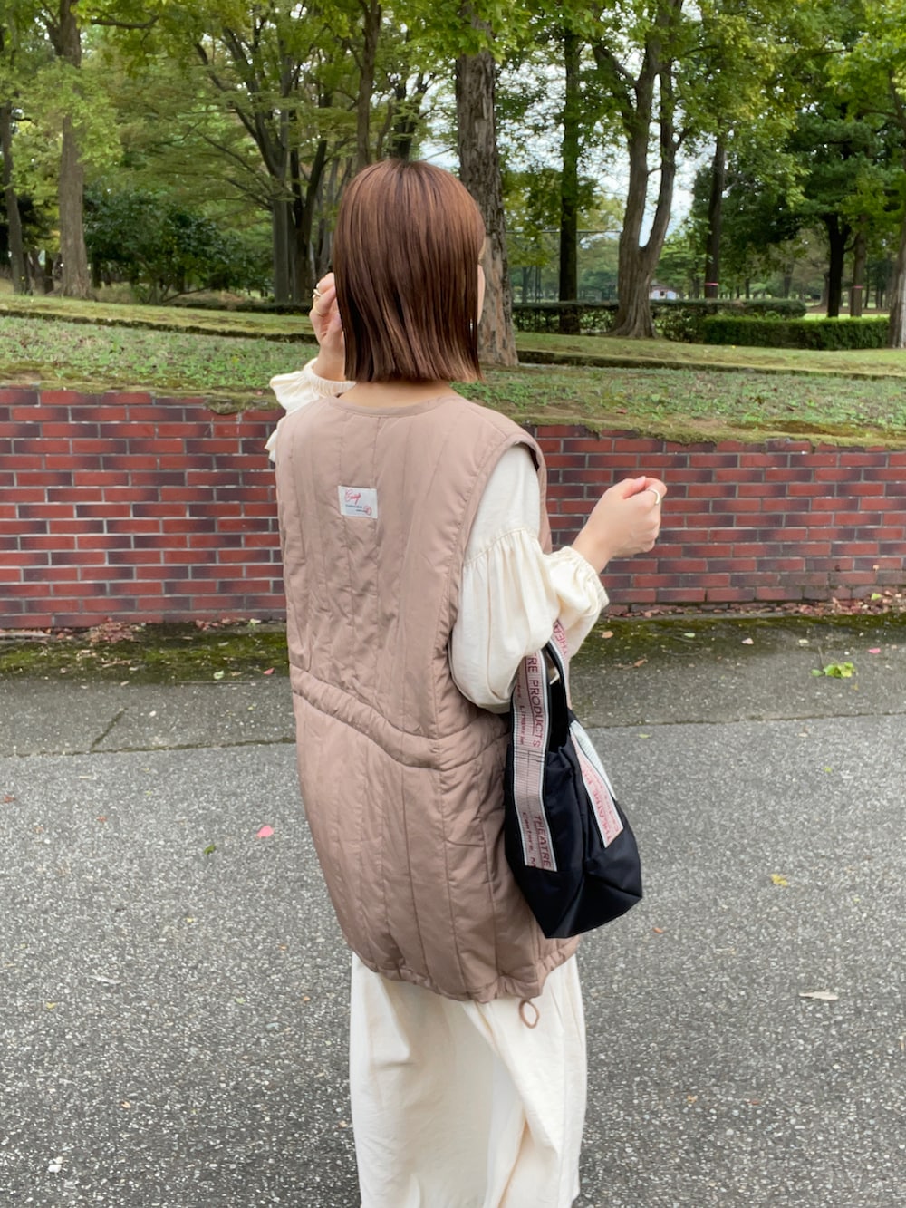 ベージュ系のベスト、ホワイト系のワンピース、ブラック系のショルダーバッグを着用したレディースの秋コーディネートの2枚目の写真